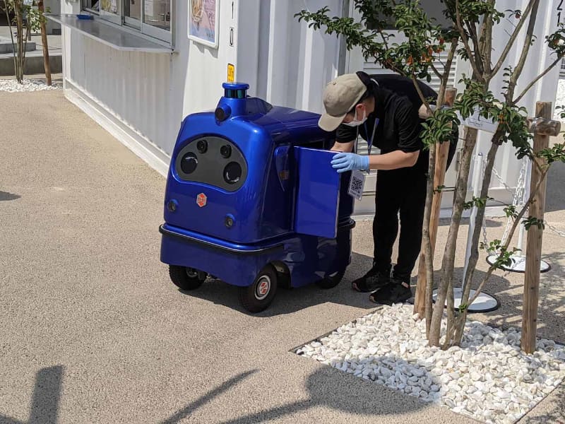 オーダーを受けた段階でDeliRoが店舗までやってきて待機し、店員が首から提げたQRコードを読ませてロボットのフタを開き、内部に商品を詰め込む