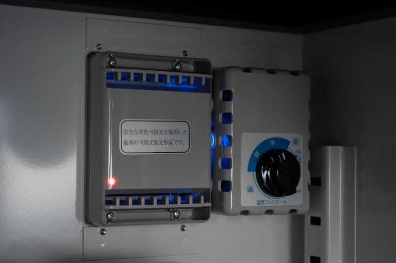 庫内から見た電子ドライユニット。赤いLEDは除湿運転中のサイン、青い光は光触媒機構のもので常時点灯している