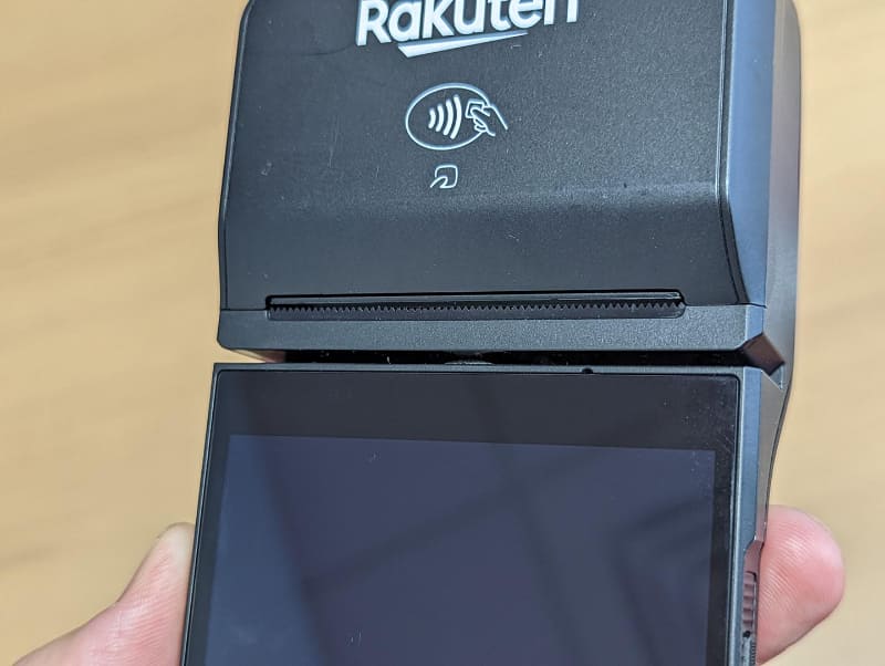 ターミナル上部の「Rakuten」ロゴの入った膨らみはプリンタのロール紙が入るスペースと非接触決済のアンテナが同居する。ディスプレイとのつなぎ目の部分にレシートの排出口と磁気カード読み取り機がある