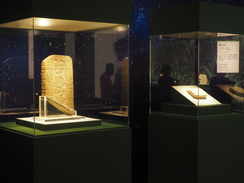 写真奥にあるのが、647年3月5日を表すマヤ文字が刻まれた《暦の文字》。マヤ文明、パレンケの忘れられた神殿から出土。手前は、1325～1521年のアステカ文明期に作られた《夜空の石板》。金星が浮かぶ夜空などが表現されている。いずれもメキシコ国立人類学博物館蔵。