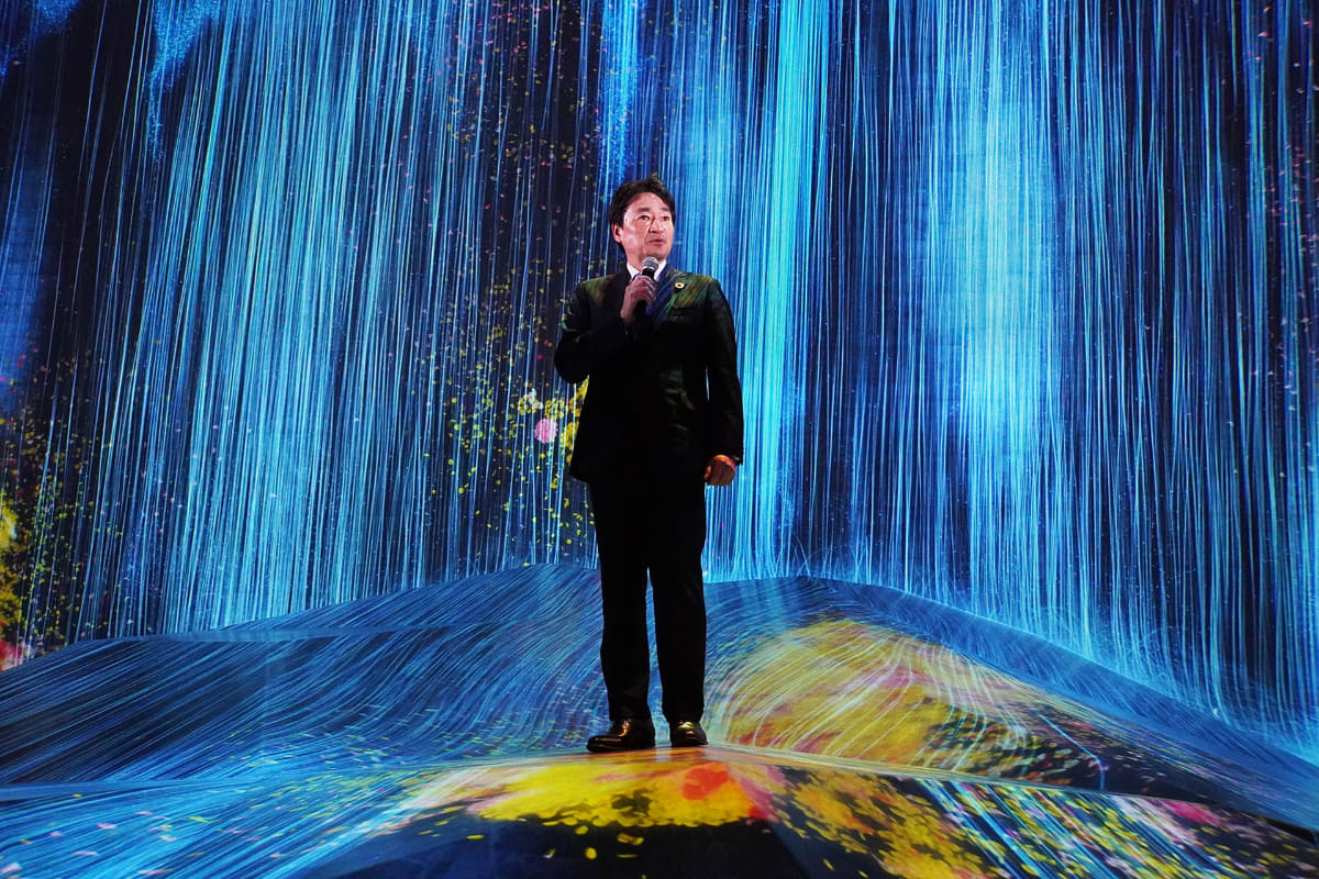 チームラボボーダレスについて説明するエプソン販売 代表取締役社長 鈴村文徳氏。この記事の1枚目と同じ場所だが、足元には黄色い花が咲いている