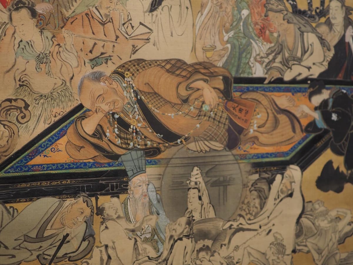 《武四郎涅槃図(部分)》には、大首飾りを首からさげ、火之用心袋を手にする松浦武四郎が描かれている。今回の特別展では、いずれも実物が、同じスペースに展示されている