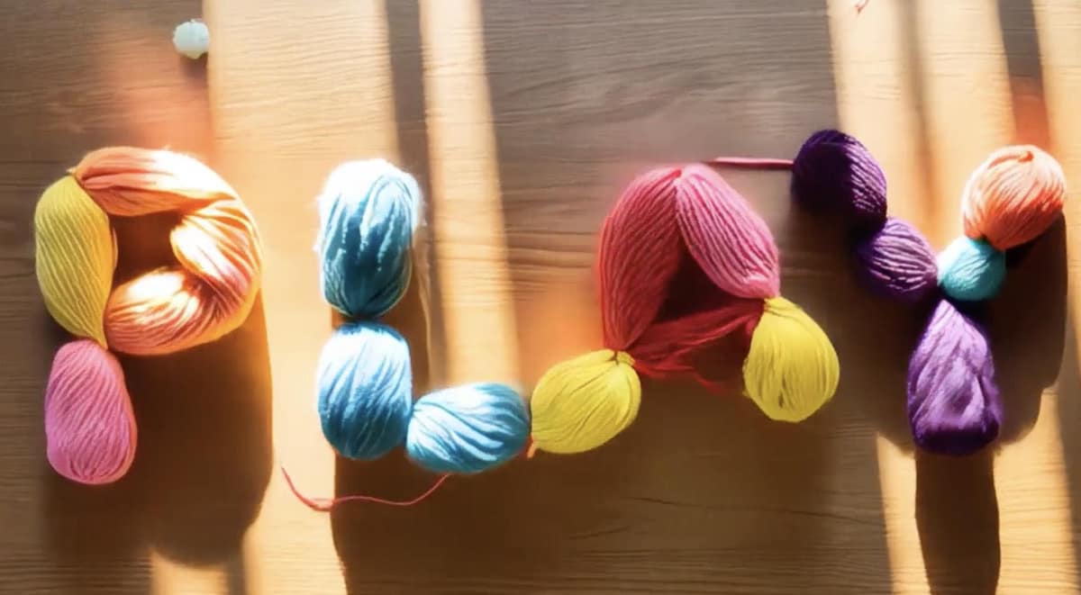 プロンプト：木製のテーブルの上の「PLAY」という文字を、2Dのカラフルな羊毛や毛糸でストップモーションアニメーション化。ゴージャスで柔らかな日差しが室内を照らしている。色は鮮やかで、素材は柔らかく、魅力的