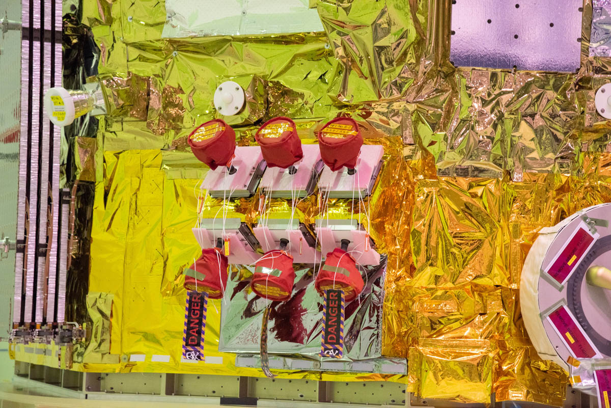 姿勢・軌道制御のためのスラスタ。3台一組のスラスタが二列、機体の4箇所に配置されている。上列スラスタの左側には姿勢制御用のスタートラッカ、その上に太陽電池パドルの展開を撮影するモニタカメラも配置された(撮影:小林伸)