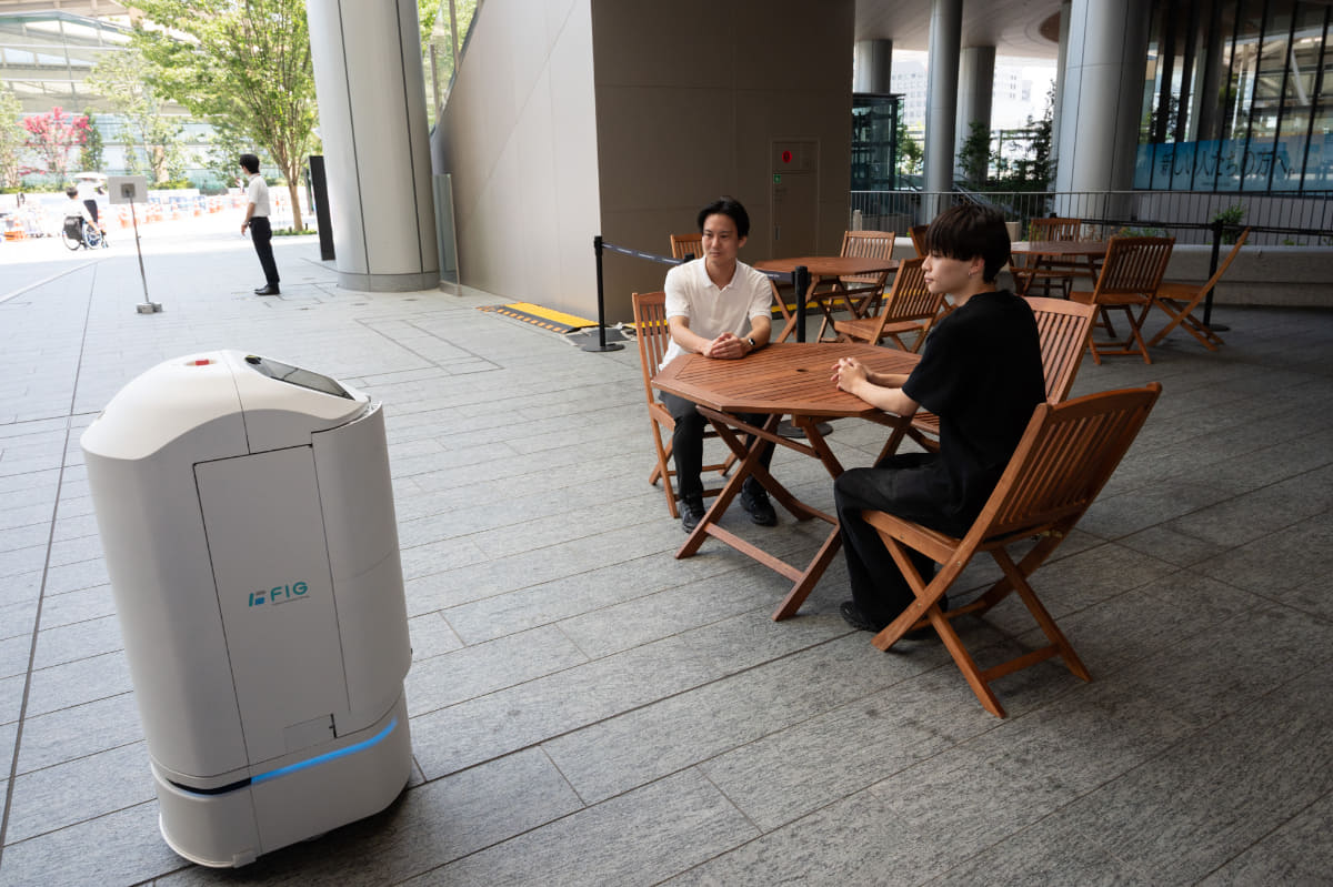 男性二人のテーブルに公共スペースで稼働するロボットが近づく