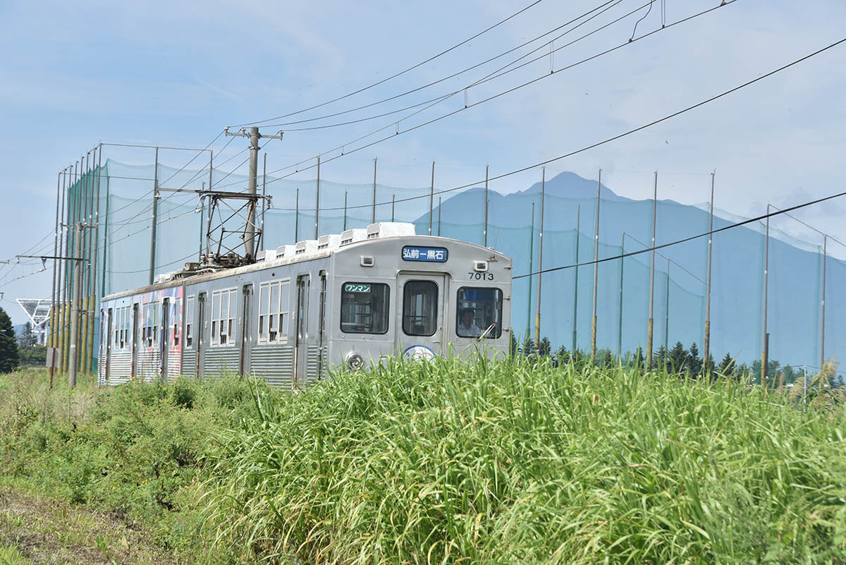岩木山をバックに運動公園前駅-新里駅間を走る弘南線の電車