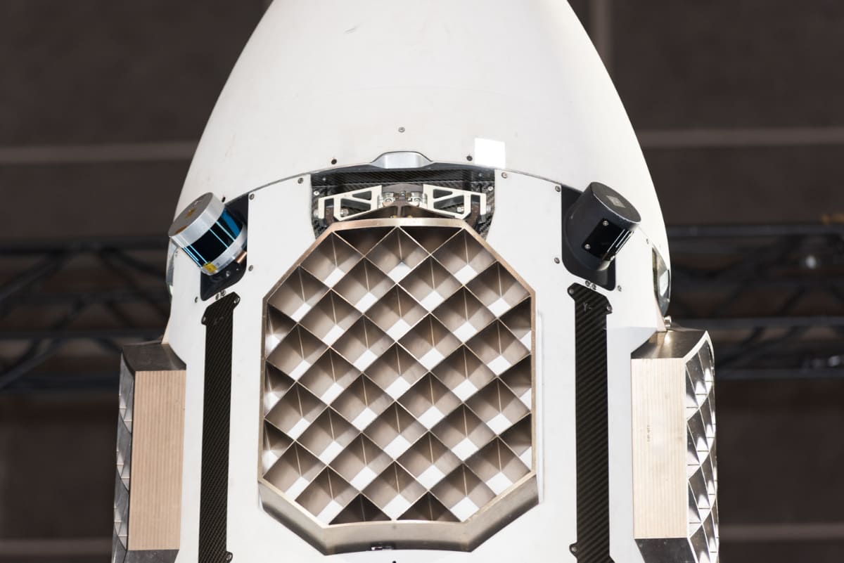 HONDAの再使用ロケット上部。着陸時の姿勢を制御する、うちわ状の制御翼(グリッドフィン)が4面に取り付けられています。制御翼の上部には、姿勢や高度を計測するセンサー類。加速度・ジャイロセンサー、LiDAR、GPSアンテナを備えているとのこと。円筒状の2種類のセンサーのうち、青いテープを撒いたようなセンサーは米Velodyne社のLiDARではないかとみられています(撮影:小林伸)