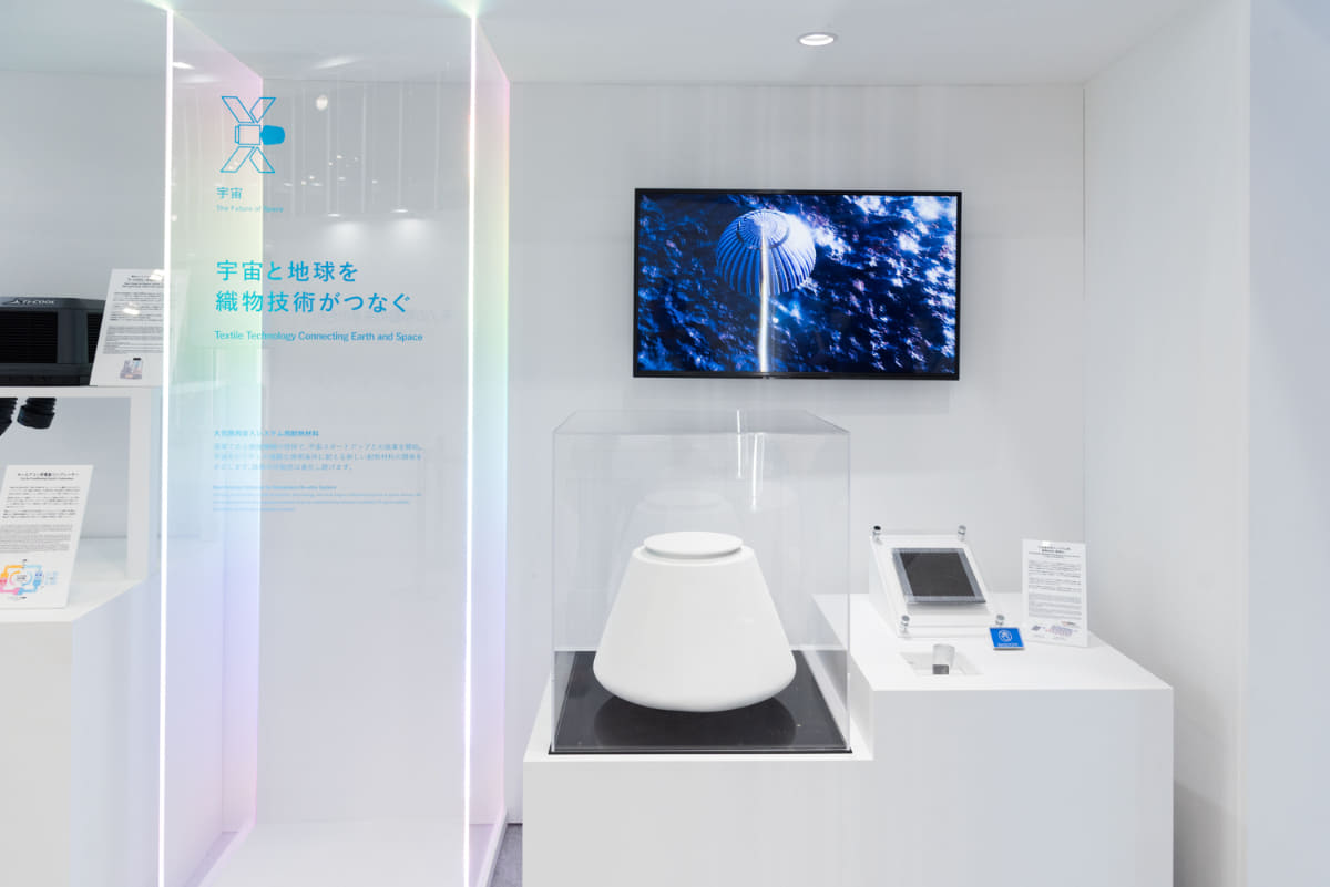豊田自動織機がElevationSpaceとともに開発する、大気圏再突入システム向けの耐熱材料(画面左は大気圏再突入カプセルの模型 右は3次元織物サンプル)(撮影:小林伸)
