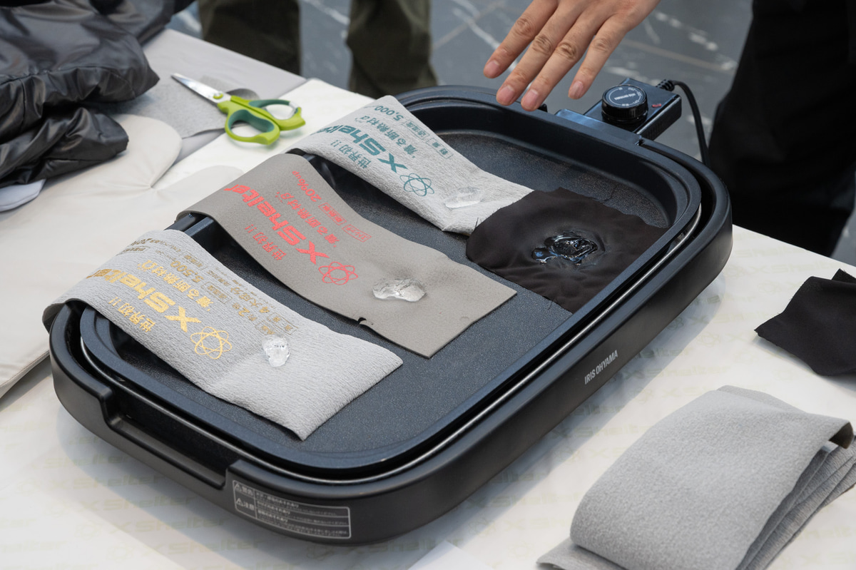200度のホットプレートの上でも氷がなかなか溶けないという「XShelter」に採用されている断熱シートの性能実験。指で触れられるほどに熱が遮断されている。右の黒い生地が通常素材で、すぐに氷が溶けてしまっている