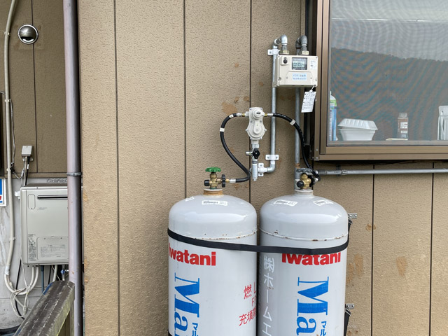 右側の窓がキッチン、ガスボンベはすぐ外。その左側に給湯器