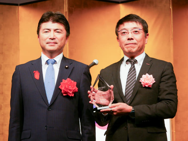 経済産業省の古賀友一郎副大臣から、経済産業大臣賞のトロフィーを受け取るNTTドコモの佐藤隆明副社長（右）