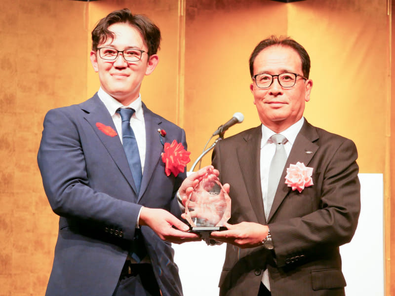 総務省 大臣政務官の川崎ひでと氏から、総務大臣賞のトロフィーを受け取るシャープの沖津雅浩社長CEO（右）