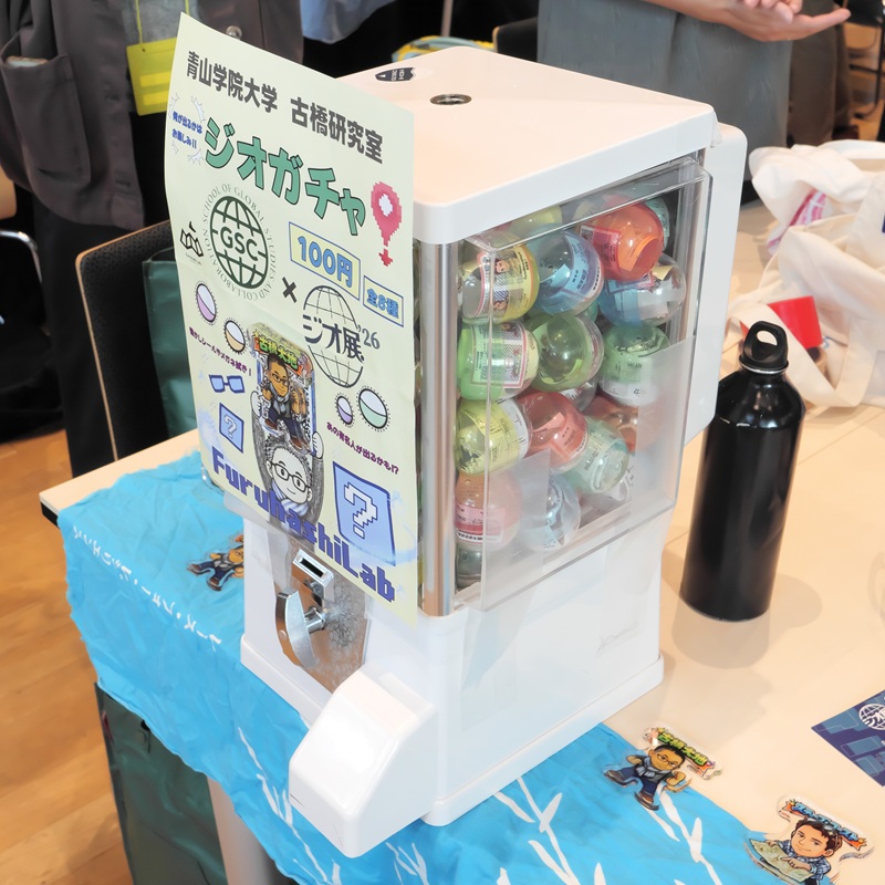 ジオ関連のグッズが当たる毎年恒例の「ジオガチャ」（青山学院大学古橋研究室）。今年の景品はジオ業界の有名人であるジョン・ハンケ氏やスティーブ・コースト氏のイラスト入りアクリルプレート