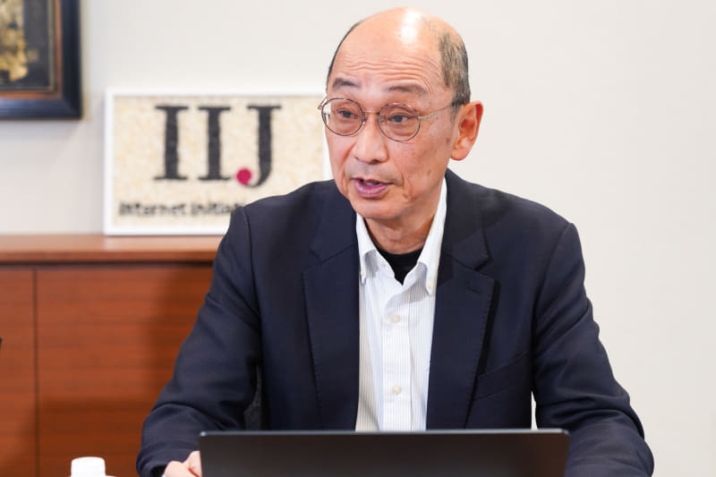 浅羽登志也（あさば としや）氏。1989年にリクルート入社。スーパーコンピュータ研究所でインターネットの研究に携わる。1992年にはIIJに1号社員として入社。初期のバックボーンネットワーク構築を担当し、BGP4に日本で初めて触れる。IPアドレス割り当てルール整備、広域LANサービス立ち上げなどにも携わり、1999年から取締役、2004年から2009年まで取締役副社長を務めたほか、2022年まで関連会社の取締役・代表取締役も歴任。現在はIIJ顧問