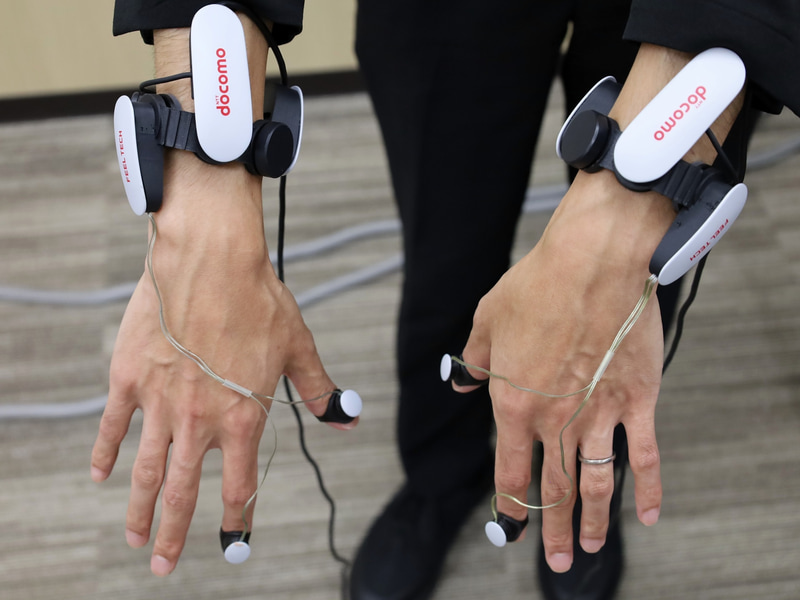 （左）装着するハプティックデバイス。（右）裏側のシリコン部分が皮膚に密着し、VRコンテンツと連動して回転することで「回転せん断刺激」が発生。あたかも腕が引っ張られたり、重さが加わったような感覚が得られる