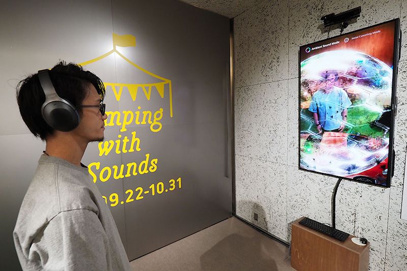 ノイズキャンセリングのAR可視化＆体験コーナー「ノイズキャンセリング ARデモ」。密閉型「WH-1000XM2」を使い、ノイズキャンセリング性能を体験することができます。画面内には、ノイズキャンセリング体験者が写り、その周囲にノイズキャンセリングのオン/オフをイメージさせる映像が表示されつつ、実際にノイズが流れます。そのノイズが、ノイズキャンセリング・ヘッドホンによりどのように除去されるのかを、映像と音で直感的に体験できるというわけです