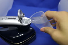 ブラシアタッチメントでホコリを払いながらシワが伸ばせる、日立の衣類スチーマー 給水用の容器を使って給水する。タンク容量は約70ml、スチーム量は約11g/分