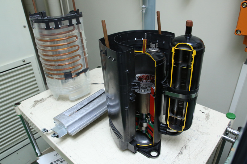 断面が見えているのがコンプレッサ。モーターでガスを圧縮するので熱が発生。コンプレッサをU字に囲むのがエネチャージシステム。コンプレッサの廃熱を蓄熱材に蓄積。霜取り運転中の熱源にする