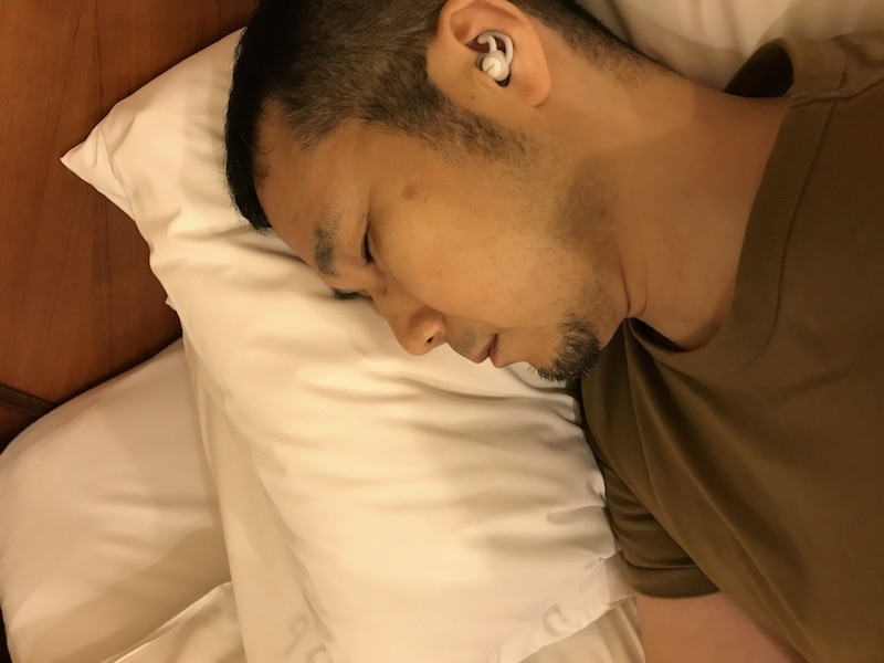 ホテルのベッドで自撮り。本体が小さく、枕に耳を押しつけるようにしても圧迫感はない。旅先での効果が検証できなかったのは本文の通り