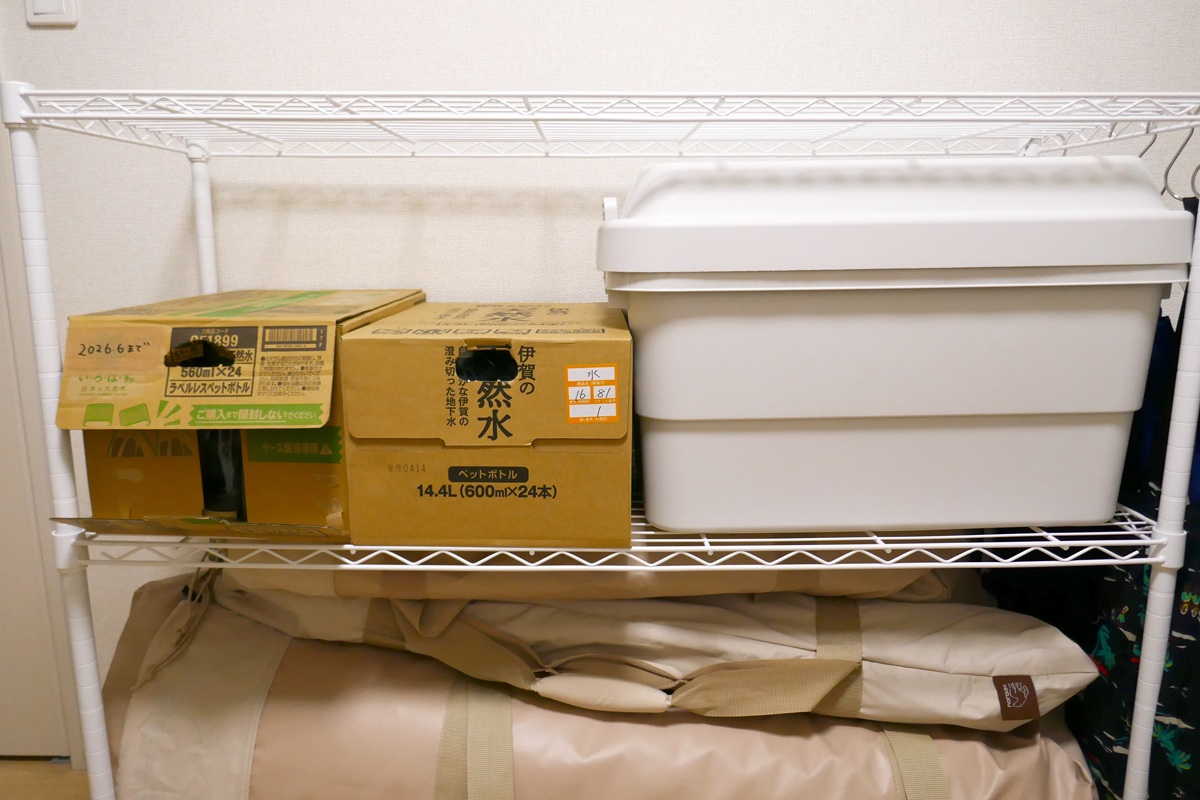 仕事机の後ろの収納棚に備蓄用の飲料水とコミックを入れたケースを収納。もともと置いてあったキャンプ道具はクローゼットに移動しました
