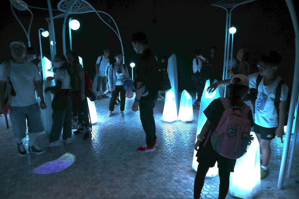 「ノモの国」は、観客一人ひとりが手にする「クリスタル」というデバイスを通じて、個別に反応する光と音の演出が楽しめる体験型パビリオンだ。照明を落とした暗い空間では視界が限られるため、来場者はより深く不思議な感覚の世界へと没入していく。そのユニークな体験に、子供たちも大喜びしている