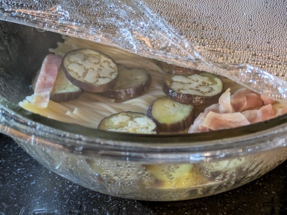 水とパスタに、ズッキーニやベーコンなどの具材を耐熱ボウルに入れて加熱する