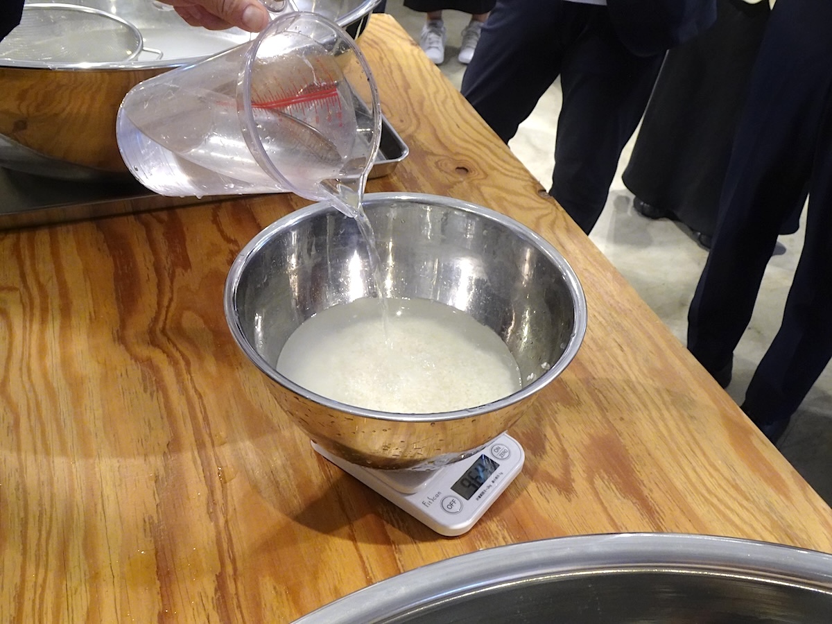 お米を洗った後に、お米の種類や炊飯方法によって適切な量の水を足す。洗米後のお米をスケールに容器ごと載せると既に重量は増えているが、容器自体の重さ＋お米の量＋必要な水の量になるように水を足していくとよい。こうすることで、洗米後のお米は必ずしもザルに上げる必要もないそうだ