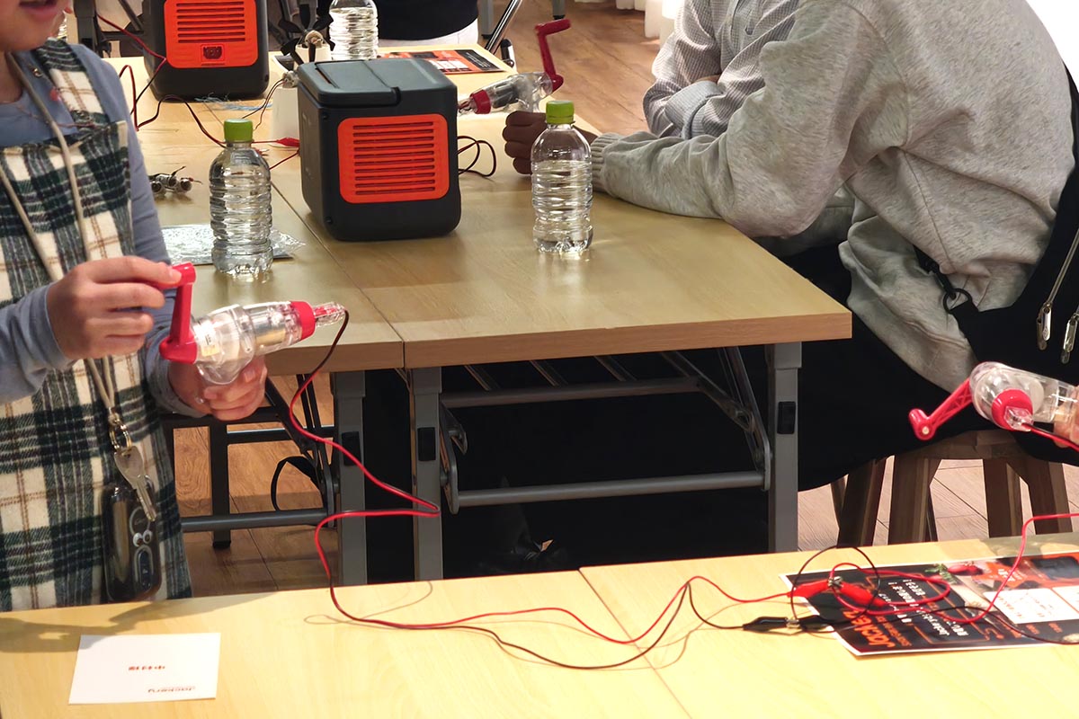 別のテーブル同士でペアを組み、手回し発電機を2台接続。片方のハンドルを回すと、もう片方のハンドルが回っていました