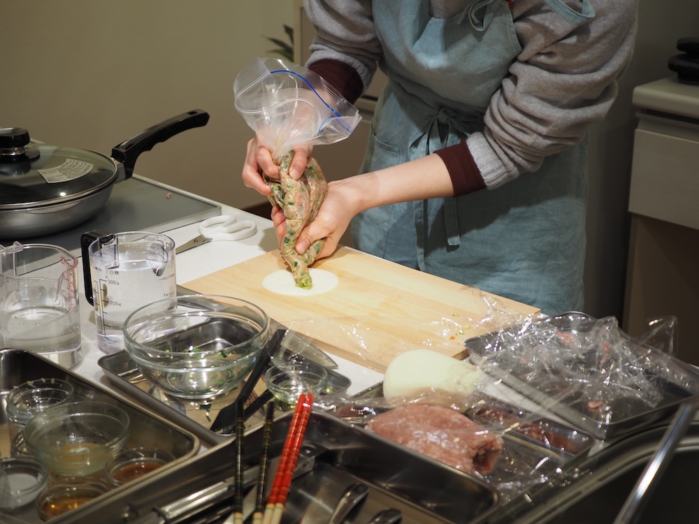 袋の端を切り、餃子の皮の上に餡を絞り出していく