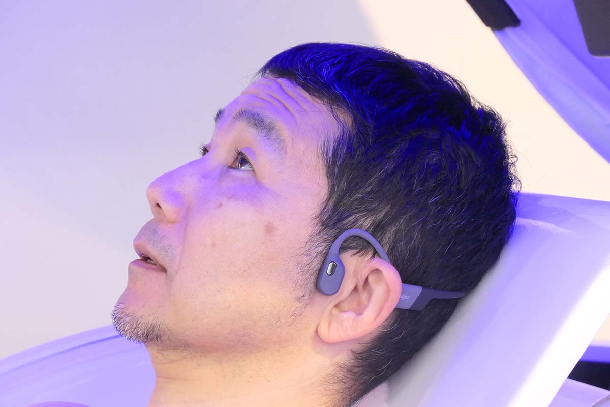 洗浄前にガイド音声や音楽が流れるワイヤレス軟骨伝導イヤホンを装着