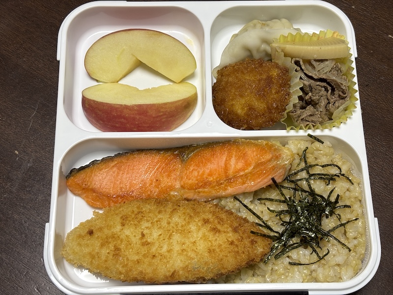 映えを気にしなければ、大は小を兼ねる(でも薄型)がラク。この日は、玄米ごはんに白身魚のフライ、焼鮭、ソースカツ、ぎょうざ、牛肉とタケノコの煮物、リンゴ。左上の雑なデザートコーナーが機内食っぽくないですか?