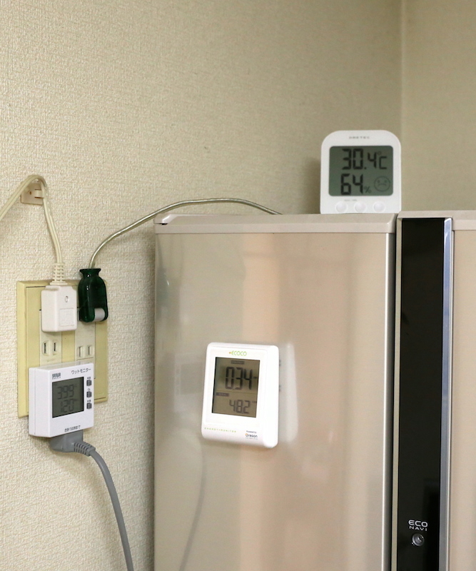 ワットモニター(左)で冷蔵庫の消費電力を計測。上部には気温を測る温度計を設置している。これらとは別に、冷蔵庫右側面の温度も計測