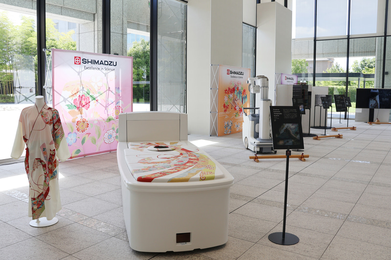 エントランスでは、創業150周年を記念し、<a href="https://www.shimadzu.co.jp/research_and_development/design_strategy/wazatowaza/">京都の伝統工芸とコラボして制作された製品</a>を展示。手前に見えるのは「TOF-PET装置」の記念モデル