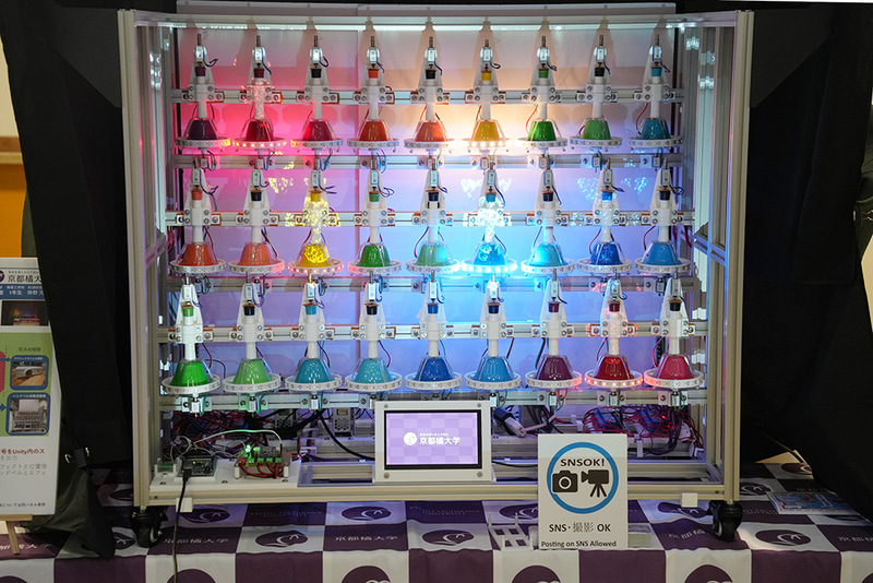 マイコン制御によるハンドベル自動演奏システム。3台のマイコンが連動し、27個のハンドベルを自動演奏しながら約500個のLEDを点滅させる。多くの機構部品は3Dプリンタで製作