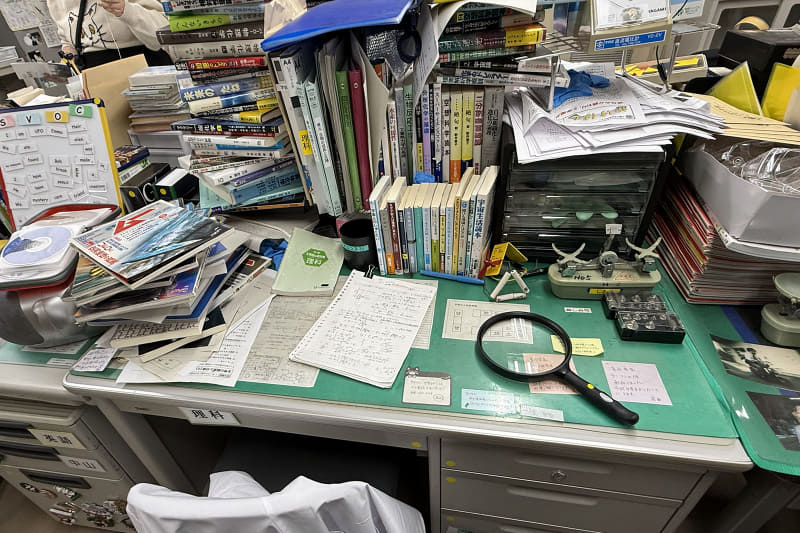 雪崩が起きそうなほど本が積まれた机（撮影：編集部）