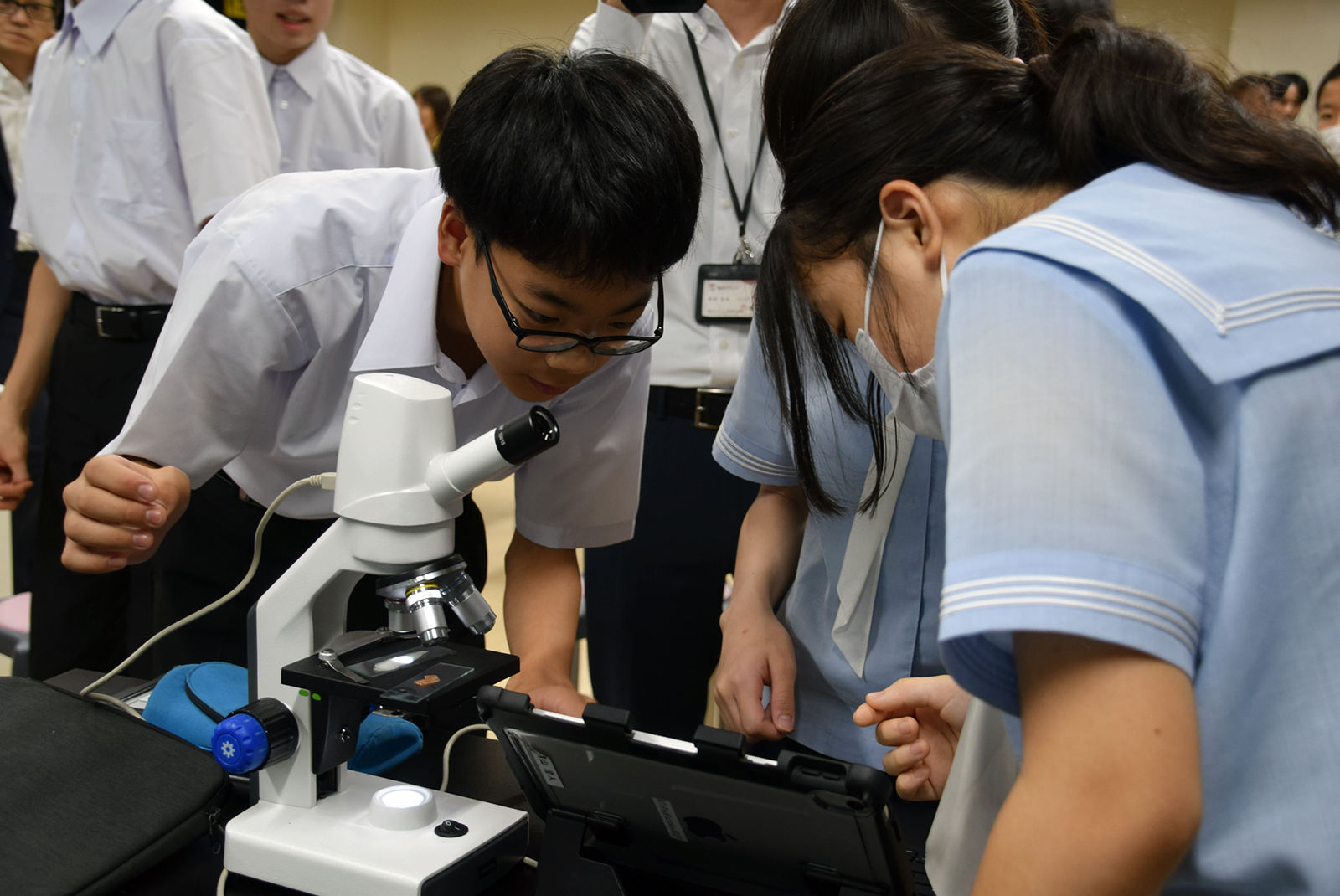 デジタル生物顕微鏡にプレパラートを載せ、ピントを合わせる。有線で接続した生徒のiPadにリアルタイムで映像が映し出されると、「見えた！」と感動の声が上がった
