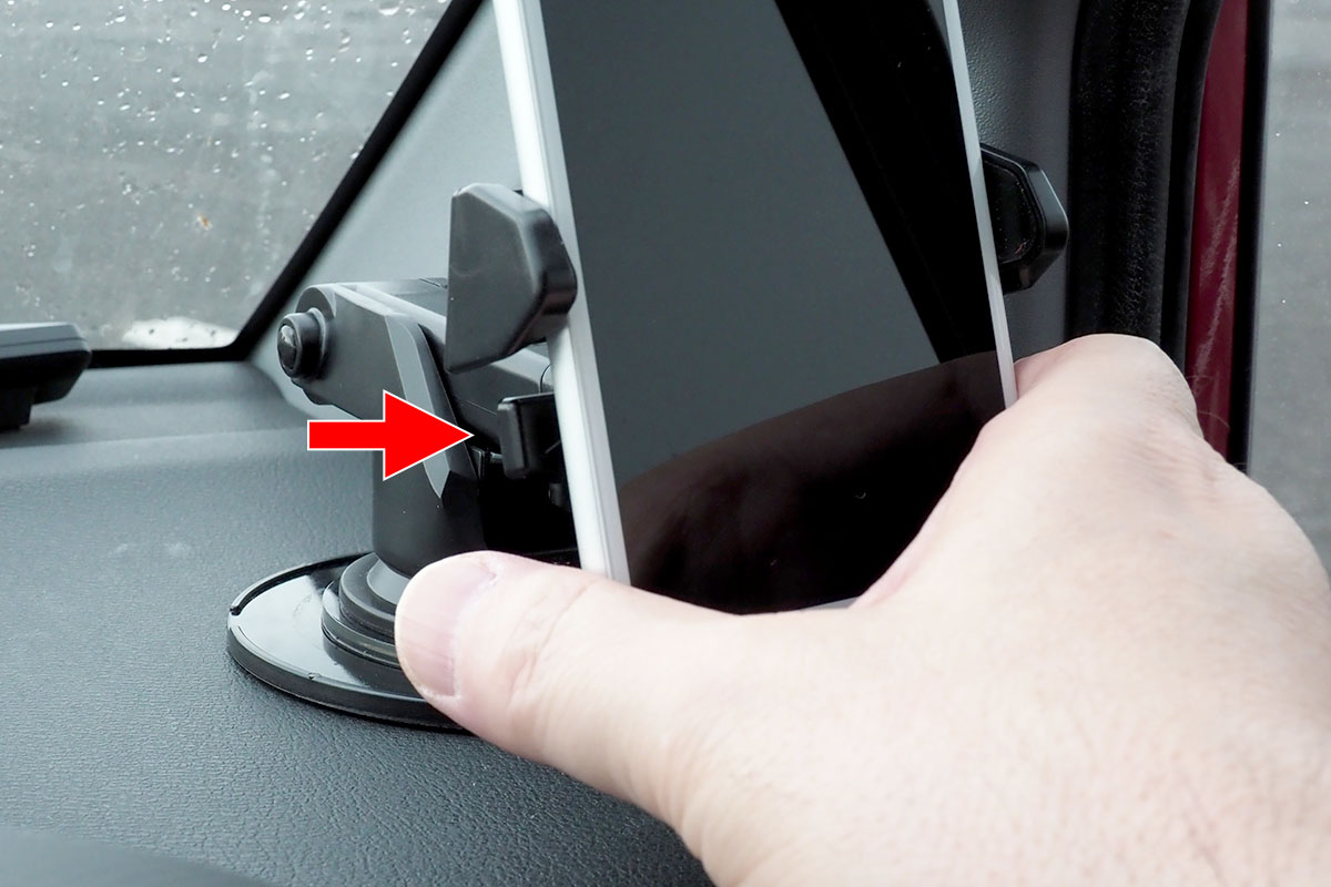 片手でホルダーから外すこともできます。赤矢印の部分を指で押すとホルダーが開きますので、そのまま端末を引き抜けばOK。その状態でホルダーが開いたまま固定されますので、再度端末をホルダーに置けば自動的に保持。脱着が片手で行える自動ホルダーというわけです。