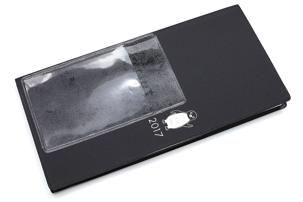 「貼るタイプのカードポケット」の一例。多くは透明の極薄樹脂製ポケットで裏面がシールになっていて、どこにでも貼って使えます。貼れば名刺やカードが入るポケットを追加できるという小物。写真ではわかりやすいように手帳の表に貼っていますが、手帳やノートなら内側に貼ることのほうが多いかしれません。でも、貼れる平面にならどこに貼ってもOK。