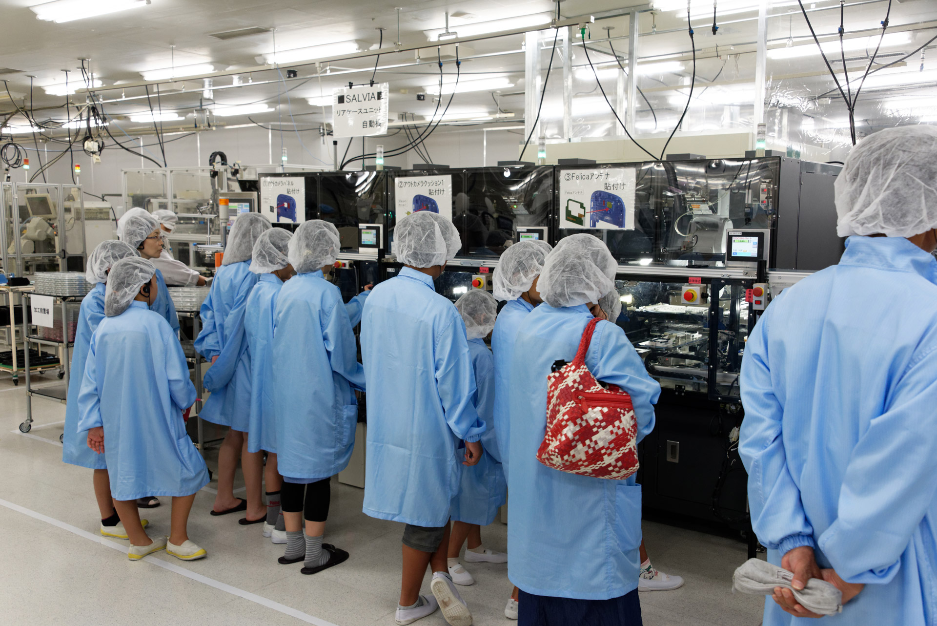 らくらくスマートフォン4の精密部品が自動で組み付けられていく機械を食い入るように見つめる子供たち