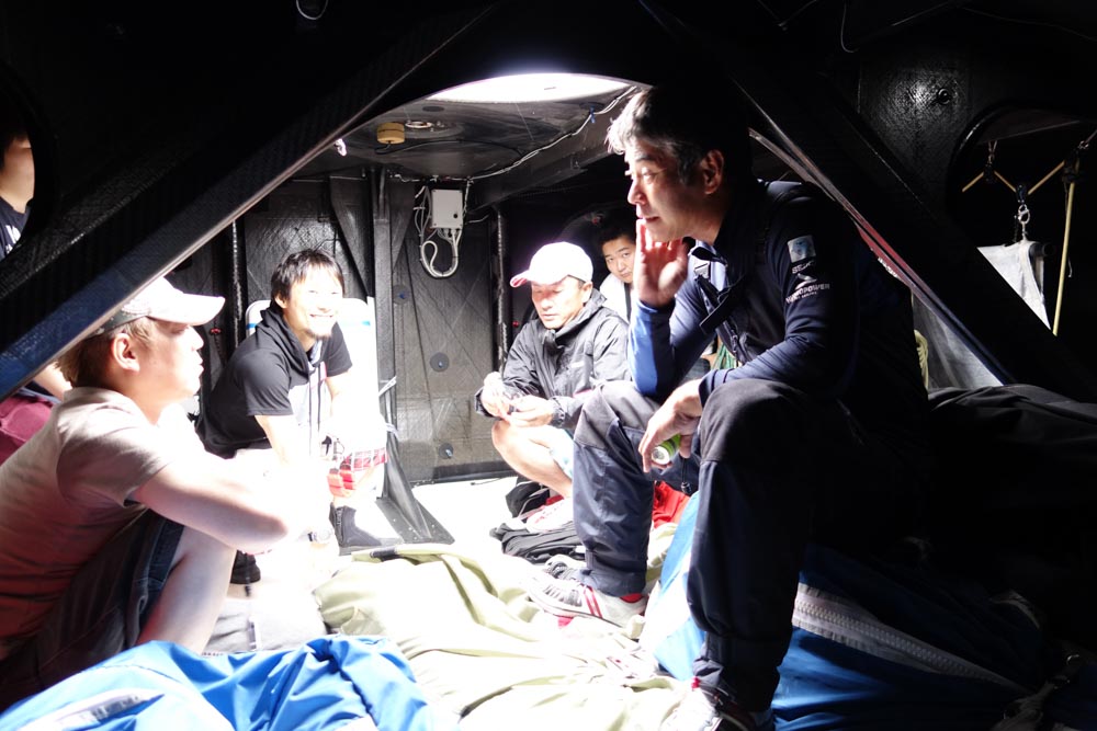 デッキ前方の帆を保管するスペース。右の白石氏が座ったり踏んだりしてるのが帆で、頭上のハッチから引き上げる