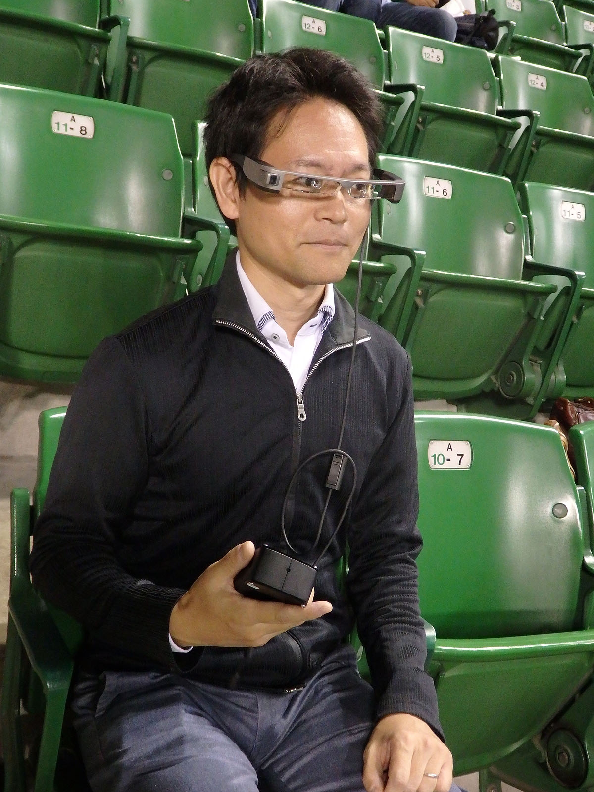 こんな感じにスマートグラスをかけて観戦。実際の試合と、スコア・解説の字幕がミックスされて見える。ちなみにモデルは筆者ではなくドコモの説明員