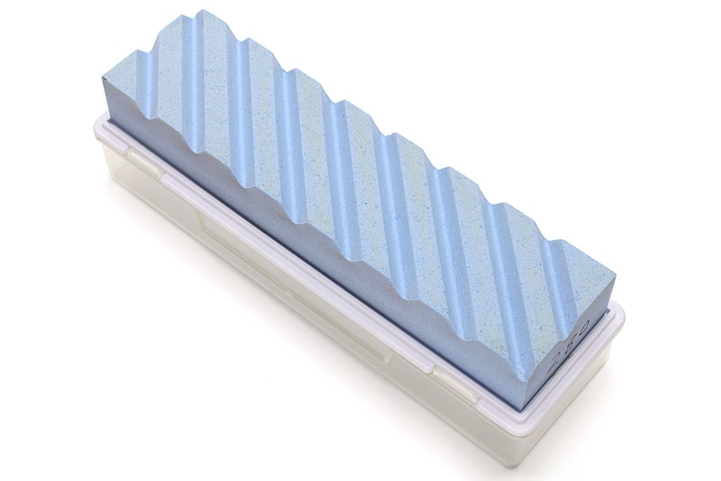 スエヒロの「修正砥石［ケース付き］ SS-2」。ケースが握り部分として役立つなど細かい部分も実用的。水をかけながら、溝が入った部分を砥石と擦り合わせ、砥石の湾曲を修正していきます。砥石表面全体に鉛筆でランダムな線を描き、修正砥石で擦っていき、鉛筆の線が消えていない箇所が「凹んでいる部分」だと判断できるので、使用時は濃い鉛筆も用意しましょう。ランダムに引いた線が均一に消えて行けば、修正完了です。