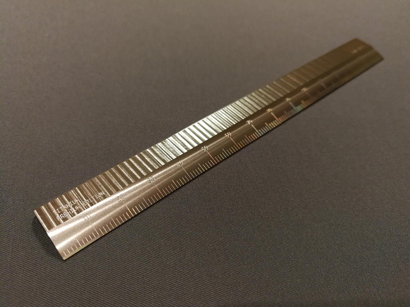 チタンの15cm定規。目盛のある上半分には、切削方向の軌跡を変えることで出来る多彩なツールマーク（切削跡）のストライプが見事に付いている
