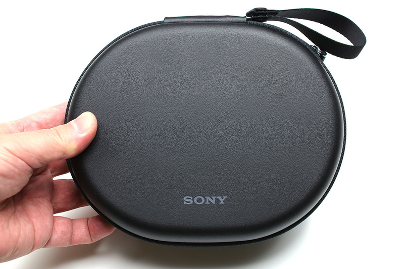 ケースの厚みは約50mm。外寸200×160mmの楕円で、意外にコンパクトに携行できます。ケース裏面には伸縮性のあるポケットが付いていて、ポータブルオーディオプレイヤーなどを入れることもできます。スナップボタンでループを開閉できるストラップが付いていて、バッグやバックパックの定位置からズレないように固定できたりしてナニゲに便利。