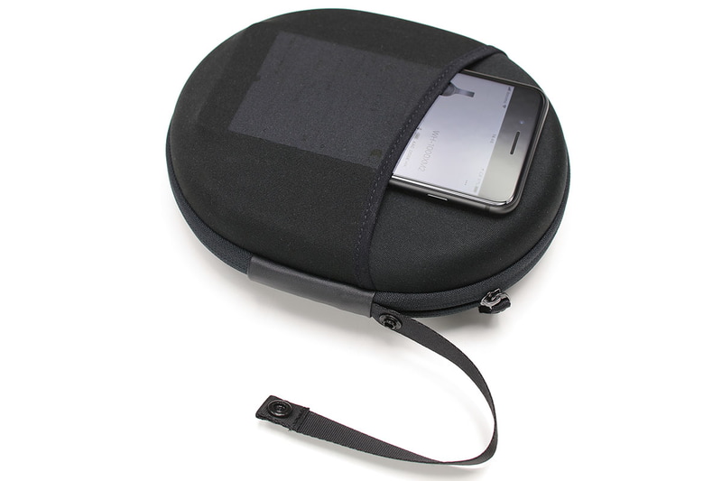 ケースの厚みは約50mm。外寸200×160mmの楕円で、意外にコンパクトに携行できます。ケース裏面には伸縮性のあるポケットが付いていて、ポータブルオーディオプレイヤーなどを入れることもできます。スナップボタンでループを開閉できるストラップが付いていて、バッグやバックパックの定位置からズレないように固定できたりしてナニゲに便利。