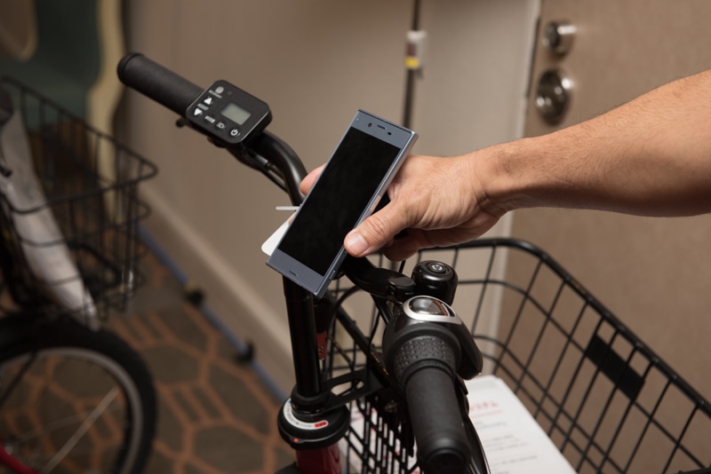 那覇市で導入が始まっているシェアサイクルは新型も展示。「ちよくる」など首都圏のサービスでも順次置き換わっていく予定という。写真はパナソニック製で、スマートフォンを充電できるUSBポートを備えているのが特徴。写真の車両は通信ユニットがまだ搭載されていない状態。ほかにブリヂストン製があり、こちらは回生ブレーキを装備するモデルになる。