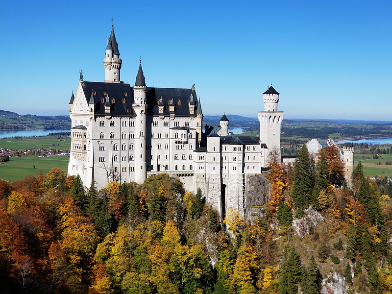 秋の紅葉とドイツのノイシュバンシュタイン城。離れた橋から望遠で撮影
