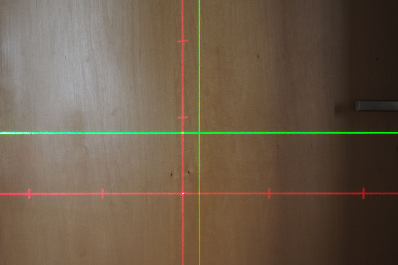 ボッシュ「Quigo 2」（左）や山真「GLZ-3-W」（中央）を使っています。右はレーザーの照射パターンで、赤色が「Quigo 2」、緑色が「GLZ-3-W」のものです。レーザー墨出し器は、置くだけで壁面などにこういった「垂直・水平を示すレーザー光のライン」が照射されます。