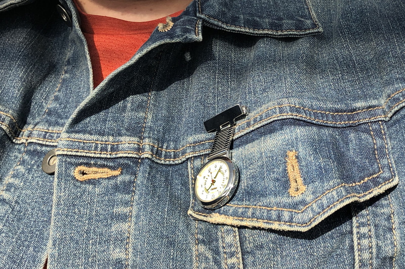 たとえばジャンパーなどにナースウォッチを装着。胸元あたりに着ければ、視線をやるだけで時間がわかります。右写真は、ナースウォッチ装着者の視点で文字盤を覗き込んだ様子。