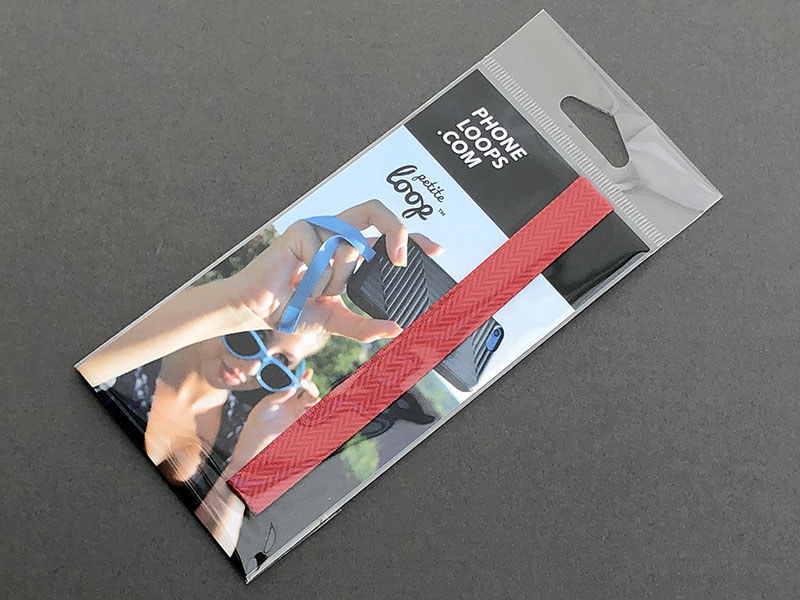 PHONE LOOPSの「PETITE LOOP」。リボンのような薄い化繊テープに両面テープが付いていて、これを端末に貼り付け、さらに市販保護ジャケットをかぶせて使うストラップです。直販価格は$4.99 USD​。